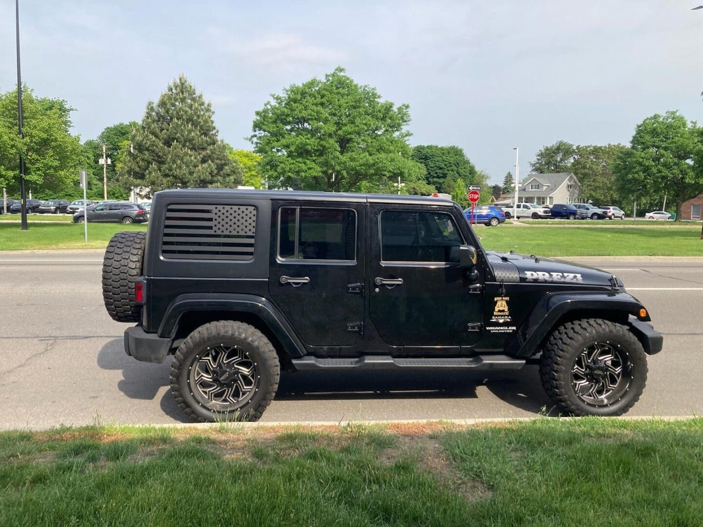 A black jeep parked in the grass near some trees.